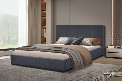 Donkergrijs gestoffeerd tweepersoonsbed met beige en bruine dekens en kussens, geplaatst in een moderne slaapkamer met ingebouwde boekenplanken en grote ramen.