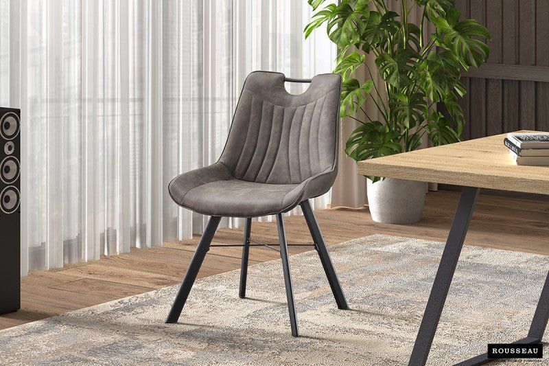 Moderne stoel met grijze fluwelen bekleding en verticale stiksels, ondersteund door zwarte metalen poten, geplaatst in een heldere kamer met natuurlijke lichtinval en groene plantendecoratie.